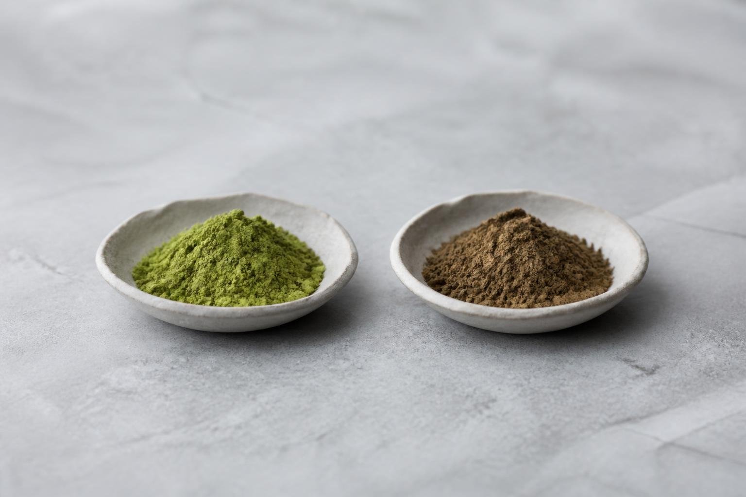 Two ceramic dishes, one of green matcha and one of brown roasted hojicha